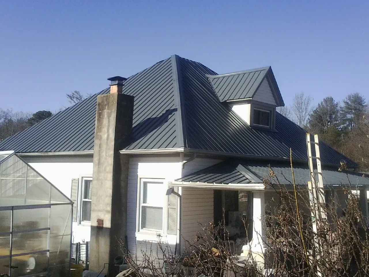 Dark blue standing seam metal roof on a white farmhouse with dormer — Slate & Tile Roof Repair by Roofing Brothers in New Haven