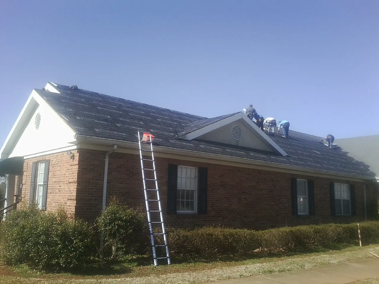 Crew tearing shingles off a brick ranch roof with a ladder set — Metal Roof Repair work by our crew in New Haven