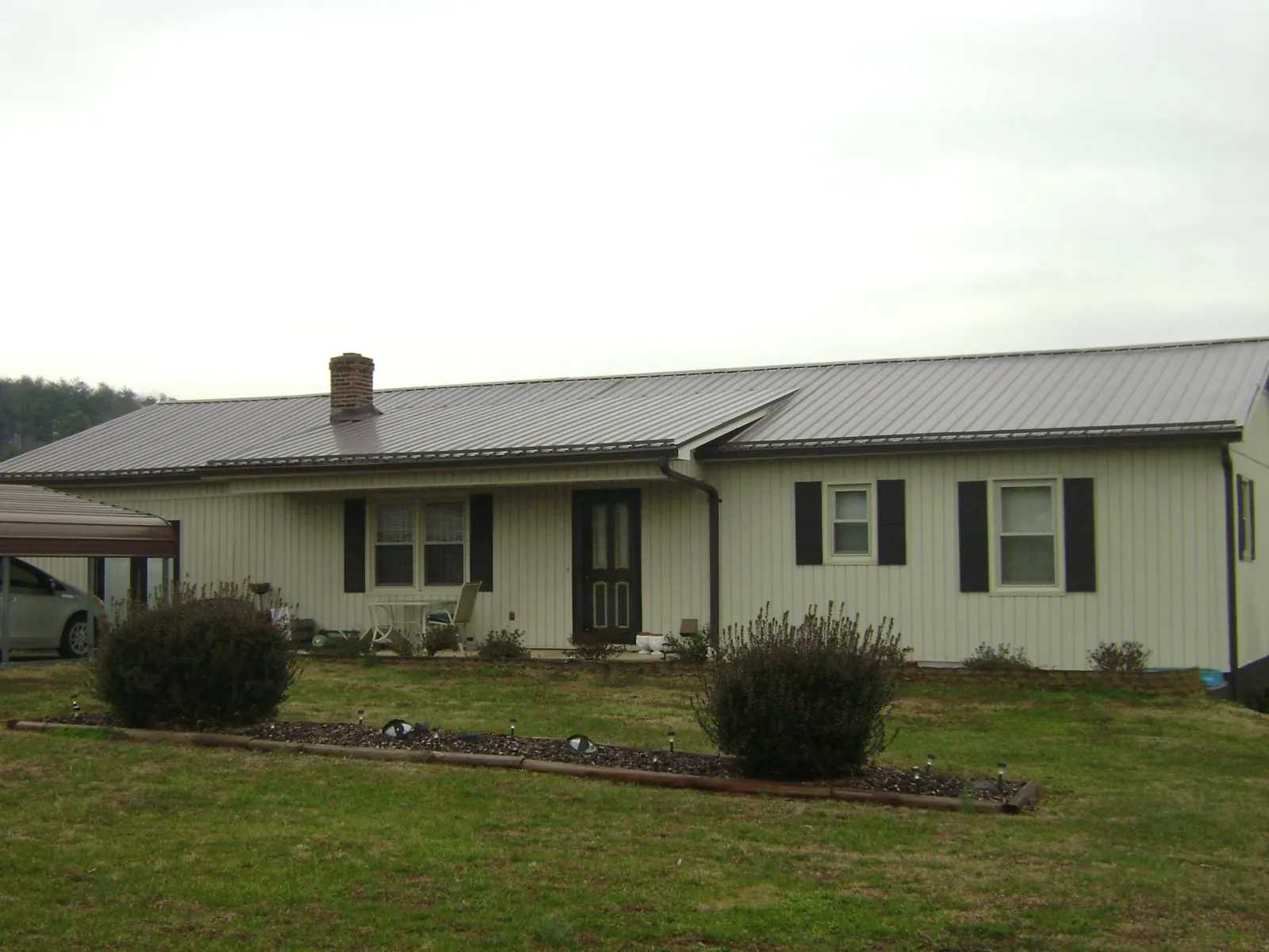 Brown metal roof on a cream sided ranch home with a brick chimney in New Haven