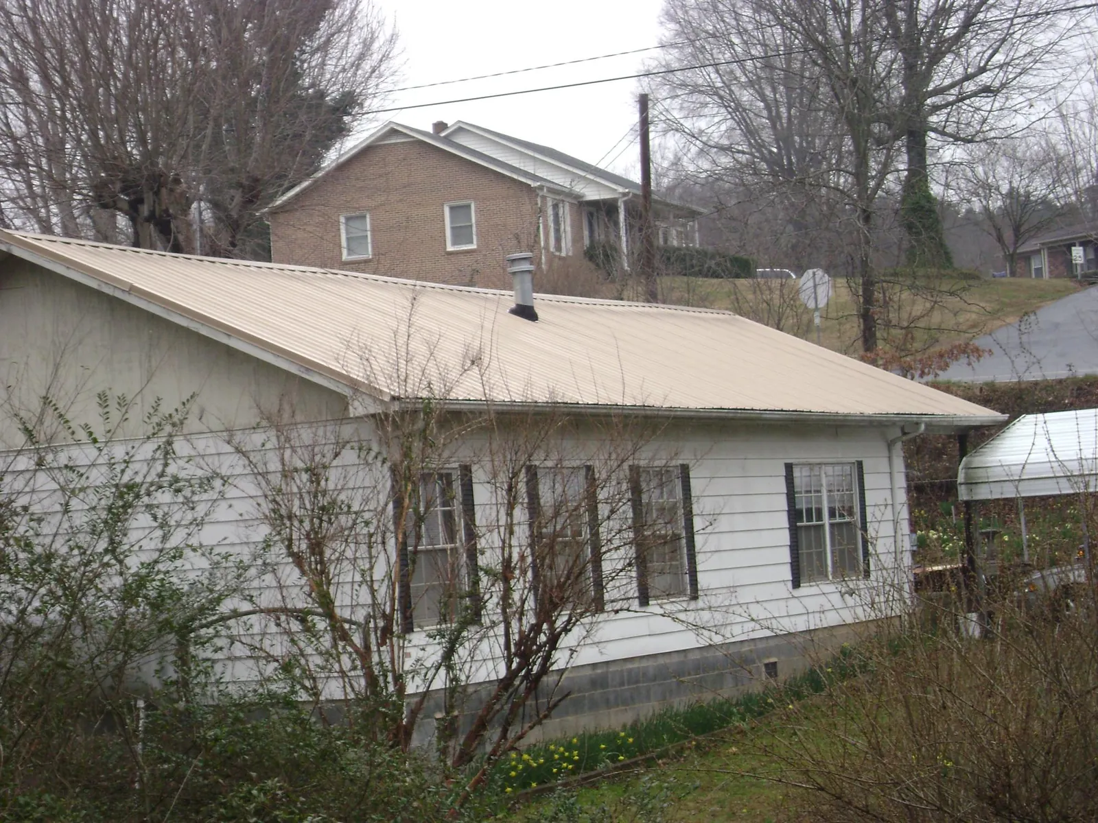 Tan metal roof on a white sided house set into a hillside — Commercial Roofing by Roofing Brothers in New Haven